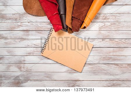 Brightly colored leather in rolls and a notebook on white wooden background. Leather craft. Copy space. Top view.
