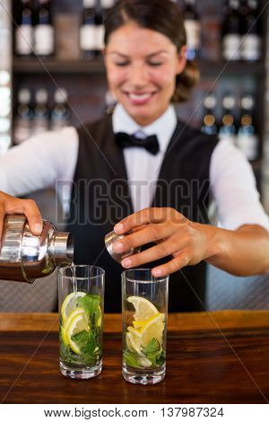 Bartender pouring a drink from a shaker to a glass on bar counter in bar