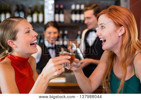 Happy friends holding a tequila shot in front of bar counter in bar