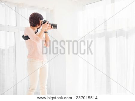 Young woman photographer working in studio. Proffessional female photographer shooting at studio. Girl taking a photo with a professional digital camera