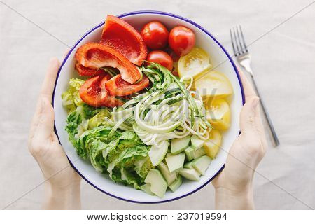 Crop Hands Holding Bowl With Sliced And Unmixed Vegetables Above White Table.