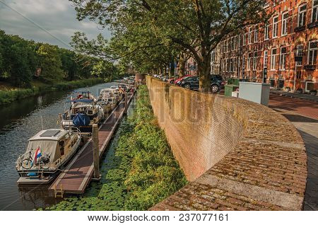 Trees, Moored Boats, Houses In Street Alongside The Dommel River And Blue Sky In The Center Of S-her