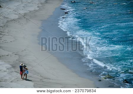 A Couple, Man And Woman, On The Shore Of A Beach Taking Pictures