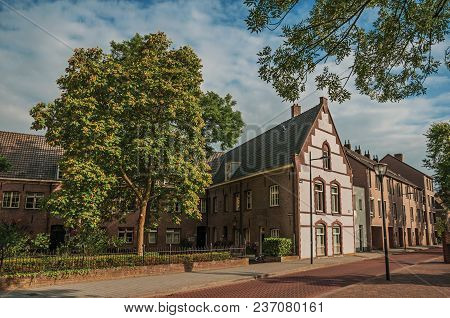 Empty Street With Large Brick House, Trees In A Garden Surrounded By Fence And Blue Sky At Sunset In
