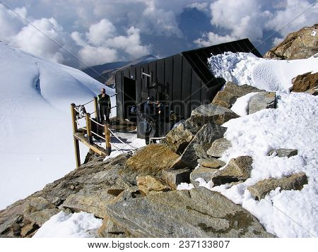 Peninne Alps, Italy, September 2011: Mountaineers Standing In Front Of Bivouac Shed.
