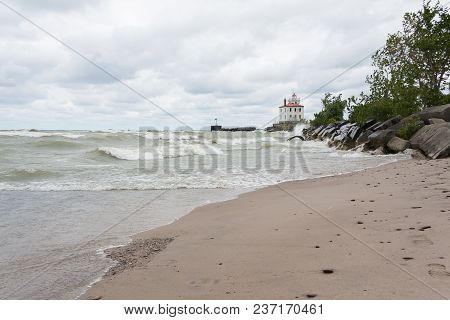 Lighthouse At Mentor Headlands Beach State Park In Ohio With Waves Crashing On Shore And Dark Clouds