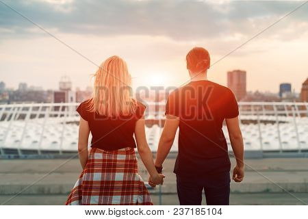 Two Lovers Embracing Overlooking The City At Sunrise Sunset. Romantic Setting.