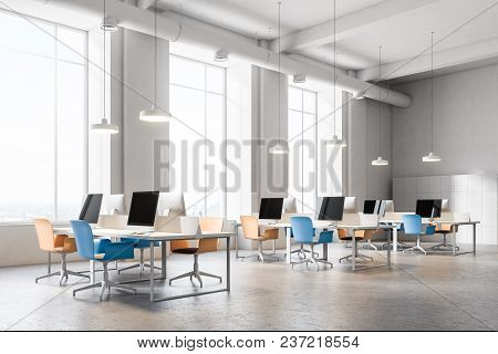 Open Space Office Corner With A Conrete Floor, Rows Of Computer Desks And Blue And Orange Office Cha