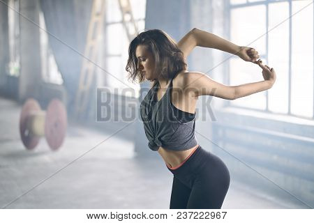 Delightful Girl In A Dark Sportswear Engaged In Yoga On The Windows Background In The Loft Style Hal