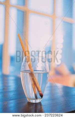 Paint Brushes In A Glass Of Water. Blue Background