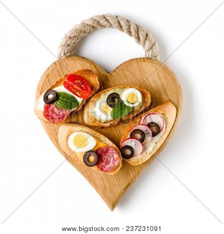 Open faced sandwich canape or crostini on a wooden serving board isolated on white background closeup. Top view.