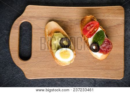 Open faced sandwich canape or crostini on a wooden serving board on dark stone  background closeup. Top view.