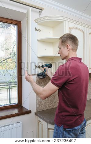 Installation Of Kitchen Furniture. The Man Is Using A Screwdriver To Adjust The Curved Door Of The C