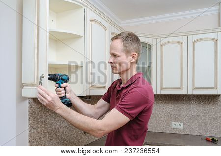 Installation Of Kitchen Furniture. The Man Is Using A Screwdriver To Adjust The Curved Door Of The C