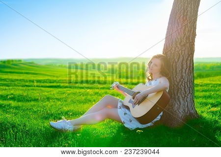 Left-handed Irl Playing Guitar Outdoor On Green Spring Grass Meadow.