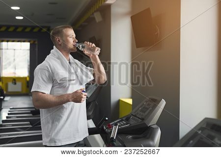 Athletic Young Man Having Rest After Running Training, Drinking Water At Gym, Standing At Treadmill,