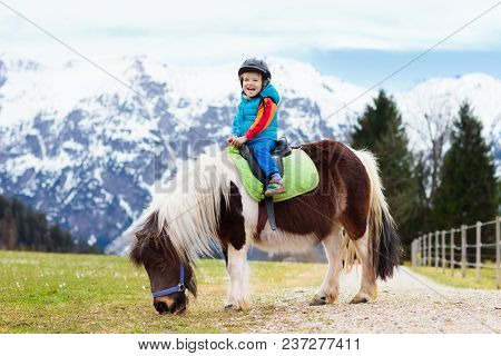 Kids Riding Pony. Child On Horse In Alps Mountains