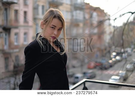 Portrait Of A Young Woman In A Black Suit Close-up Against A Background Of A Blurry City In The Rays