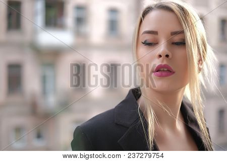 Portrait Of A Young Woman In A Black Suit Close-up Against A Background Of A Blurry City In The Rays