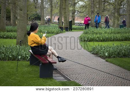 Lisse, Netherlands - April 20, 2018: Woman In Yellow Sweater Sitting In The Botanical Garden Of Keuk