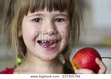 A Cute Little Curly Toothless Girl Smiles And Holds A Red Apple. Portrait Of A Happy Baby Eating A R