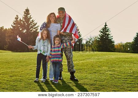 Shot Of Patriotic Family. Soldier With His Wife And Daughters With American Flags.