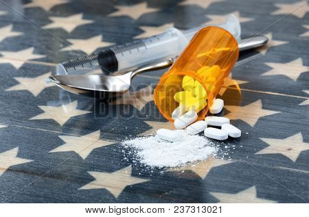 Front View Of Opioid Pain Killer Tablets With Spoon And Syringe On Rustic Usa Flag In Background For