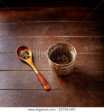 Green tea (sencha) in a traditional, japanese tea cup and sencha leaves on a wooden  tea spoon. Dark wooden background. 