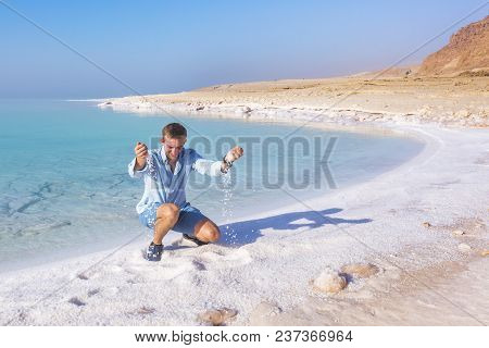 Ttourist Throws Salt Sitting On The Shore Of The Dead Sea. Jordan Landscape