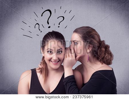 A teenager girl looking confused with drawn question marks above the head, while a girlfriend whispers something in her ear concept.