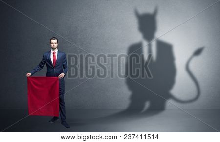 Businessman standing with red cloth in his hand and devil shadow on the background