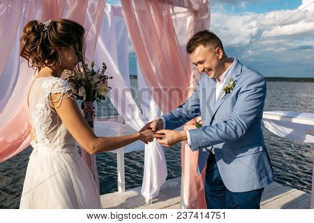 The Bride And Groom Exchange Rings On The Pier In The Middle Of The Lake
