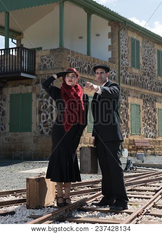 Young Couple With Vintage Suitcase Standing On The Trainlines Outside ,  Looking And Waiting For The