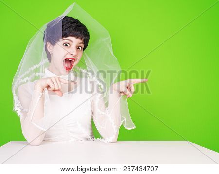 Caucasian Fiancee In White Dress Pointing To The Side. Young Fiance Sitting At A White Table Pointin