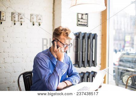 Man In Glasses Professional Writer Talking On Mobile Phone While Sitting With Laptop Computer In Cof