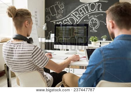 Rear View Of Concentrated Coders Using Computer And Analyzing Computer Program Script While Working 
