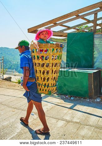 Kyaiktiyo, Myanmar - February 16, 2018: The Porter Walks Along The Street, Carrying Little Girl In B