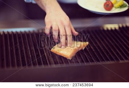 Master chef hands cooking grilled salmon fish with potatoes on a restaurant kitchen