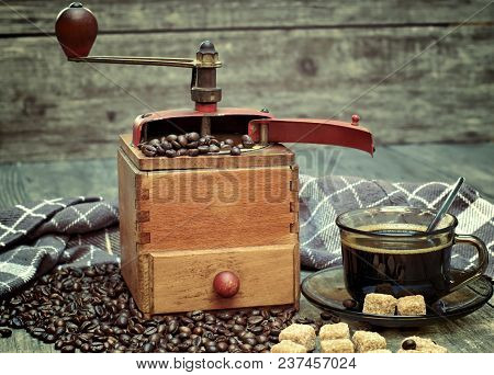 Old Coffee Grinder With A Cup Of Coffee, Coffee Beans On A Wooden Background.