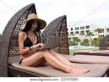 Work And Travel. Incredibly Sexy Girl In A Black Bikini Sits With A Laptop Near The Pool. Find A Tou