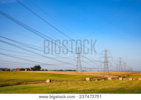 Summer rural landscape with wrapped hay bales on a field and high-voltage power lines in Scotland UK