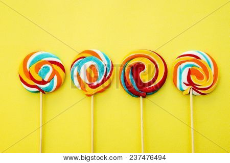 Colorful Hard Candy Lollipop On Yellow Pastel Background. Rainbow Sweet Pattern On Stick Flying Arou