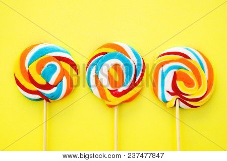 Colorful Hard Candy Lollipop On Yellow Pastel Background. Rainbow Sweet Pattern On Stick Flying Arou