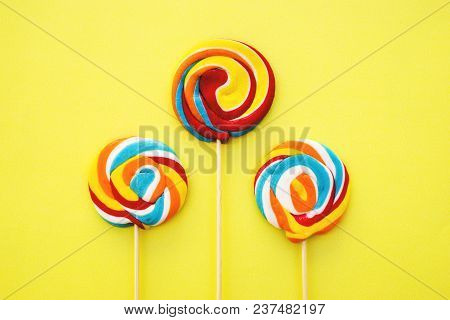 Colorful Hard Candy Lollipop On Yellow Pastel Background. Rainbow Sweet Pattern On Stick Flying Arou