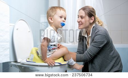 Portrait Of Young Mother Talking To Toddler Son While He Is Using Toilet