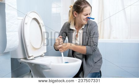 Portrait Of Woman Feeling Disgust And Bad Smell Cleaning Toilet At Home