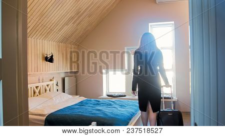 Rear View Silhouette Photo Of Young Woman With Suitcase Enetering Hotel Room With Big Window