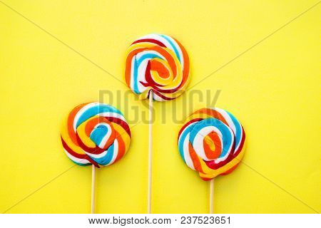 Colorful Hard Candy Lollipop On Yellow Pastel Background. Rainbow Sweet Pattern On Stick Flying Arou