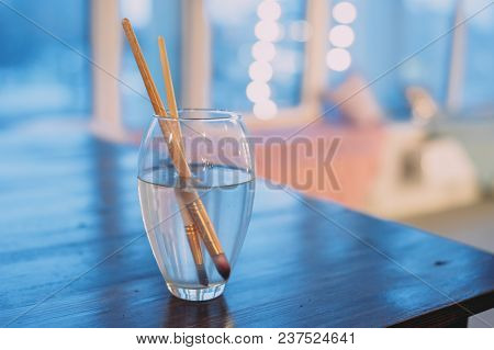 Paint Brushes In A Glass Of Water. Blue Background