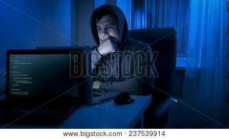 Man In Hoodie Looking On Laptop Screeen At Night